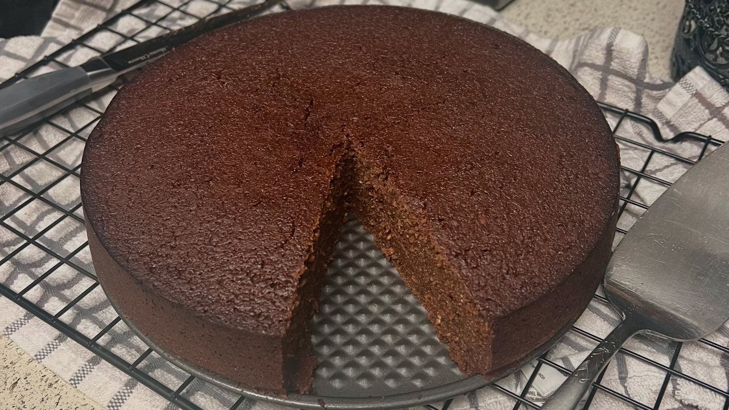 Caribbean Black Cake with a slice cut out and kitchen utensils in the background