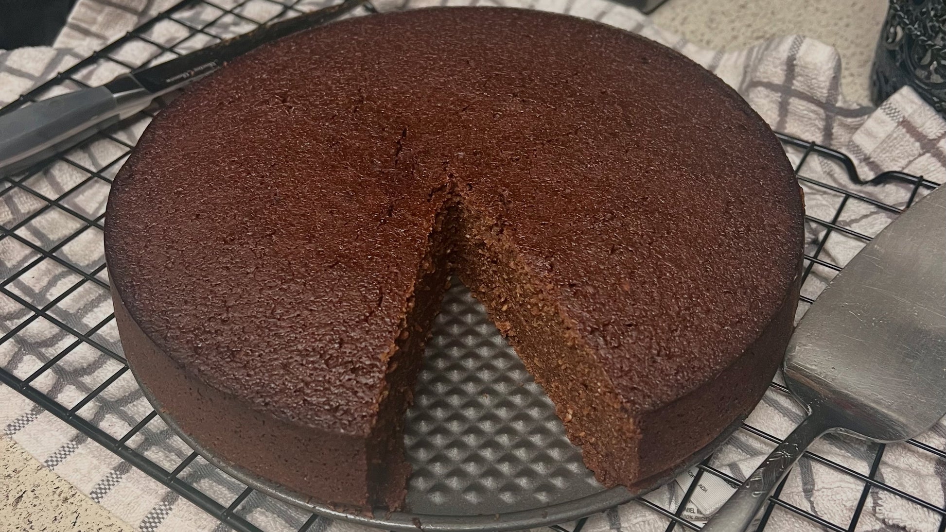 Caribbean Black Cake with a slice cut out and kitchen utensils in the background