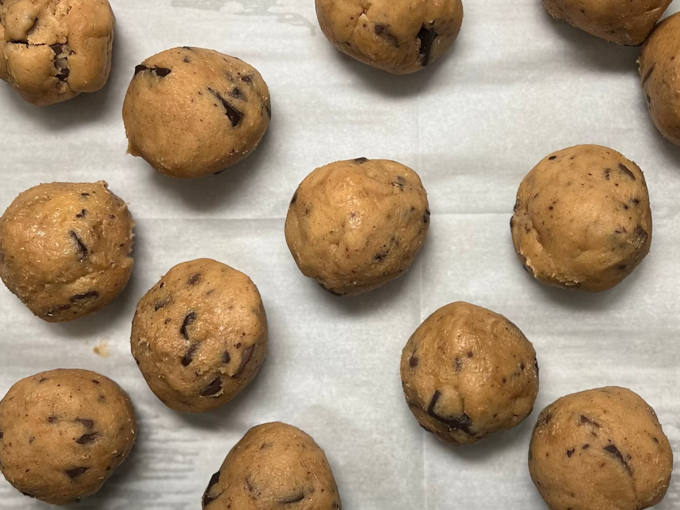 Baked chocolate chip cookies on a baking tray lined with parchment paper.